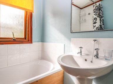 A bathroom with a bathtub a sink two glasses a mirror and a window with an orange blind at Lodge Two Country View Park in Graveney