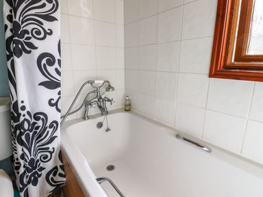 A bathtub with a faucet and handheld shower next to a window with a black and white patterned shower curtain at Lodge Two Country View Park Graveney