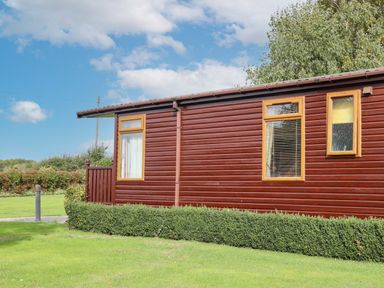 A brown wooden cabin with three windows and green hedges in front at Lodge Two Country View Park Graveney