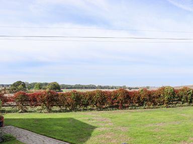 A garden with a trimmed hedge and green grass with fields and trees visible in the distance at Lodge Two Country View Park in Graveney