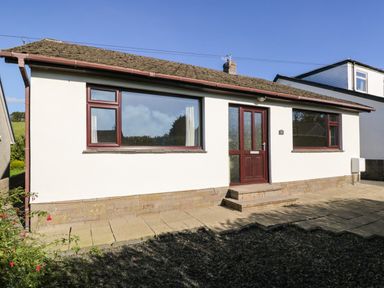The front exterior of a single-story house with a tiled roof two windows a front door and a paved walkway at Marsh Garth in Kirkby-In-Furness