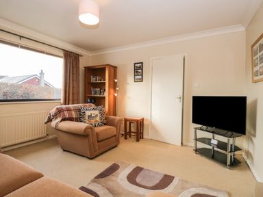 A living room with an armchair, a bookshelf, a television on a stand, and a window at Marsh Garth Kirkby-In-Furness