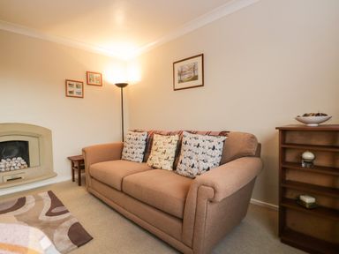 A living room with a beige sofa a floor lamp a fireplace and framed pictures on the wall at Marsh Garth in Kirkby-In-Furness