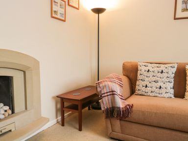A living room corner with a beige sofa and patterned cushions next to a wooden side table and a tall floor lamp at Marsh Garth in Kirkby-In-Furness