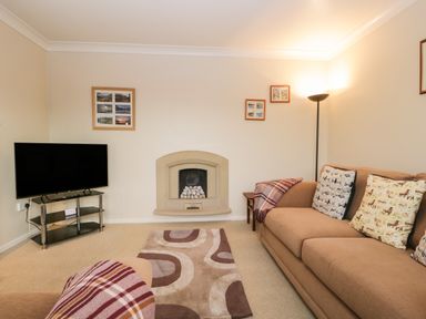 A living room with a beige sofa and a patterned rug a television on a stand and a fireplace at Marsh Garth in Kirkby-In-Furness