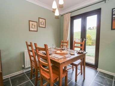 A dining room with a wooden table and chairs near glass doors overlooking a garden at Marsh Garth in Kirkby-In-Furness