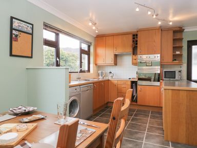 A kitchen with wooden cabinets a dining table chairs and appliances at Marsh Garth in Kirkby-In-Furness
