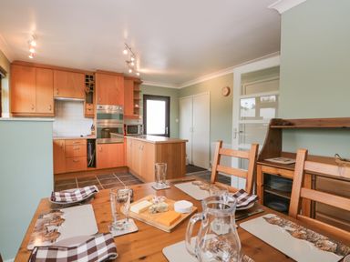 A kitchen and dining area with wooden cabinets and a table set with placemats and cheese at Marsh Garth in Kirkby-In-Furness