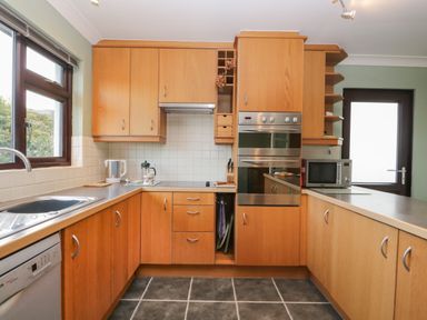 A kitchen with wooden cabinets a dishwasher a microwave oven and a window at Marsh Garth in Kirkby-In-Furness
