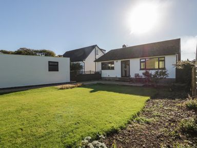 A backyard with a lawn, a patio with a table and chairs, and two white houses at Marsh Garth in Kirkby-In-Furness
