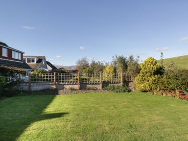 A backyard with a lawn and shrubs bordered by a wooden fence at Marsh Garth in Kirkby-In-Furness