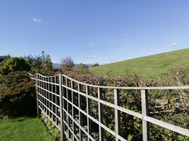 A wooden trellis fence with bushes and grass with a hill and blue sky in the background at Marsh Garth in Kirkby-In-Furness