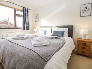 A bedroom with a large bed topped with folded towels two bedside tables with lamps and framed pictures on the walls at Marsh Garth in Kirkby-In-Furness