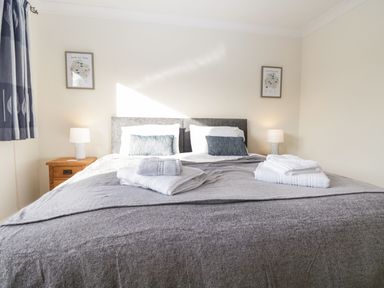 A bedroom with a large bed with gray bedding two bedside tables with lamps and folded towels on the bed at Marsh Garth in Kirkby-In-Furness