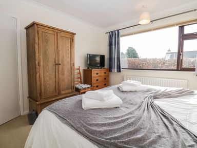 A bedroom with a bed covered in blankets and towels a wooden wardrobe a dresser with a TV and a chair near a window at Marsh Garth in Kirkby-In-Furness