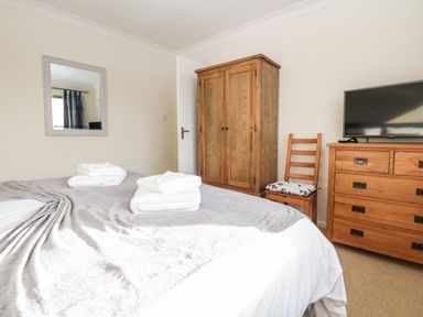 A bedroom with a bed covered in white and gray linens wooden wardrobe wooden dresser chair with cushion and a wall mirror at Marsh Garth in Kirkby-In-Furness