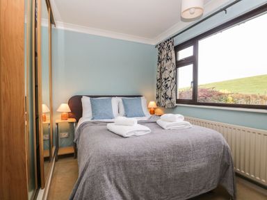 A bedroom with a bed covered in grey bedding and folded towels near a window at Marsh Garth in Kirkby-In-Furness