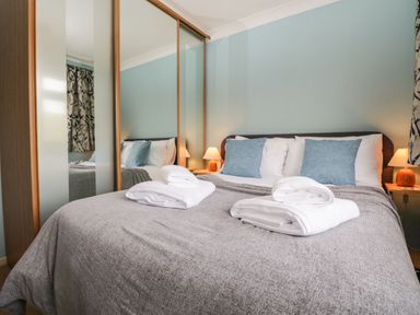 A bedroom with a bed made with grey bedding and blue pillows with folded white towels on top at Marsh Garth in Kirkby-In-Furness