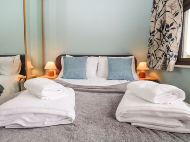 A bedroom with a bed, two blue pillows, bedside lamps, folded white towels and a window with patterned curtains at Marsh Garth in Kirkby-In-Furness