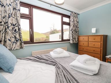A bedroom with a bed and folded towels with a wooden dresser near the window at Marsh Garth in Kirkby-In-Furness