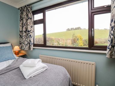 A bedroom with a bed with folded towels on it and a window showing a view of a green hill at Marsh Garth in Kirkby-In-Furness