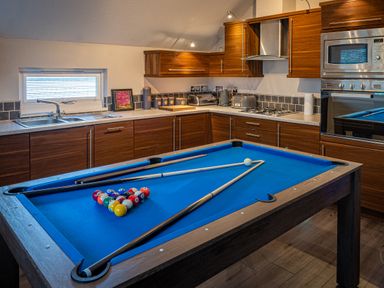 A kitchen with wooden cabinets a blue pool table and billiard cues at Lakeland Lodge in Carnforth