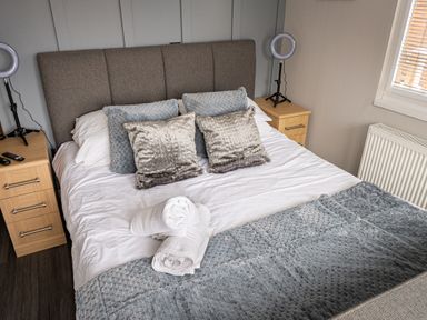 A bedroom with a bed with pillows and rolled towels on it and bedside tables with ring lights at Lakeland Lodge in Carnforth