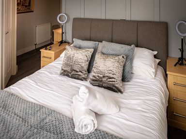 A bedroom with a bed, pillows, rolled towels, bedside tables, and ring lights at Lakeland Lodge in Carnforth