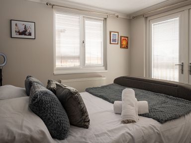 A bedroom with a bed with pillows and rolled towels by windows with blinds at Lakeland Lodge in Carnforth