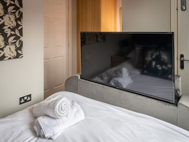 A bedroom with a bed holding rolled towels and a TV on a stand at Lakeland Lodge in Carnforth