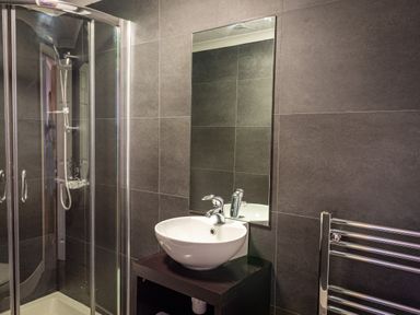 A bathroom with a glass shower enclosure a white sink on a black stand a rectangular mirror and a chrome towel rail at Lakeland Lodge in Carnforth