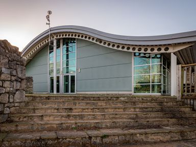 An exterior view of a modern building with a curved roof and stone steps leading up to glass doors at Lakeland Lodge in Carnforth