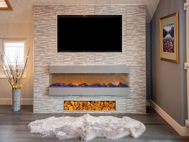 A fireplace with stacked firewood below and a television mounted above in a room with a soft rug on the floor at Lakeland Lodge in Carnforth