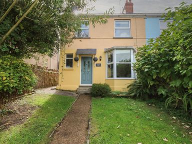 The front exterior of a two-story house with a blue door, bay window, and garden path at Greengate in Tenby