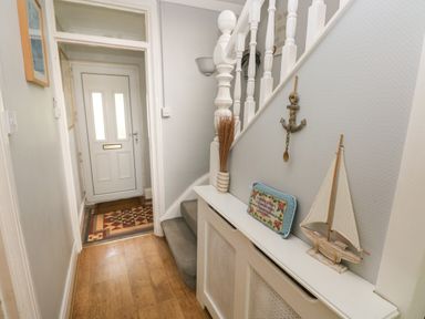 A hallway with a white front door a wooden floor stairs with a gray carpet and nautical decorations at Greengate in Tenby