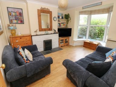 A living room with two dark blue sofas a fireplace a wooden chest and a bay window with blinds at Greengate in Tenby