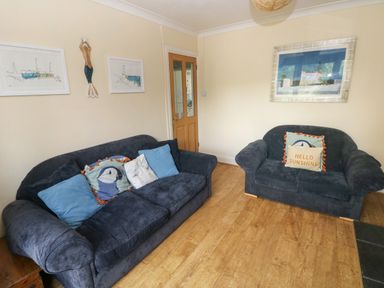 A living room with two dark blue sofas with cushions and framed pictures on the walls at Greengate in Tenby