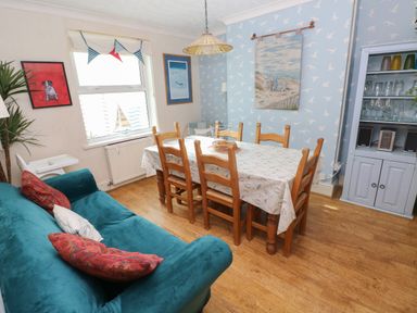 A dining room with a wooden table and chairs a teal sofa and a cabinet with glasses at Greengate in Tenby