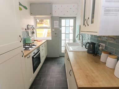A kitchen with white cabinets a sink countertop appliances and a door leading outside at Greengate in Tenby