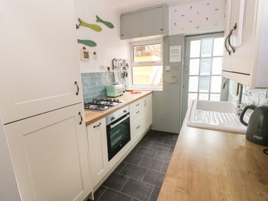 A narrow kitchen with white cabinets wooden countertops a gas stove a toaster and a kettle at Greengate in Tenby