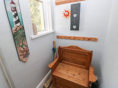 A corner with a wooden bench and hooks on walls with a lighthouse wall hanging and a window at Greengate in Tenby