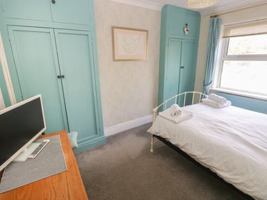 A bedroom with a bed with folded towels a desk with a monitor and blue cupboards at Greengate in Tenby