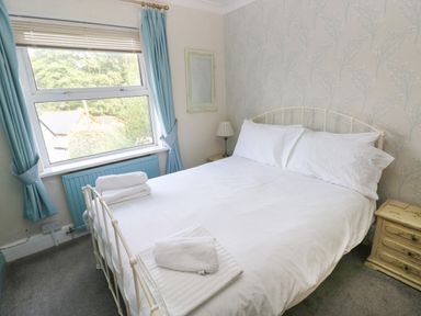 A bedroom with a double bed white bedding bedside tables and a window with blue curtains at Greengate in Tenby
