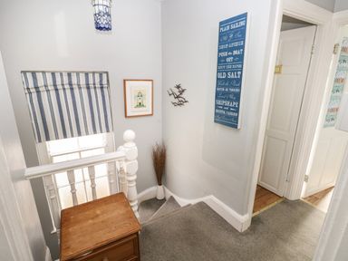 A stairway landing with a wooden chest, wall decor, a window with striped blind and carpet at Greengate in Tenby