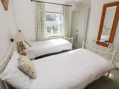 A bedroom with two single beds a small bedside table with a lamp a window with curtains a wardrobe and a full length mirror at Greengate in Tenby