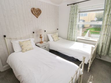 A bedroom with two single beds a nightstand with a lamp a window with curtains and a heart-shaped wall decoration at Greengate in Tenby