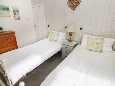 A bedroom with two single beds bedside table with lamp wooden dresser and coastal paintings at Greengate in Tenby