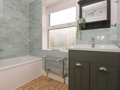 A bathroom with a bathtub sink cabinet and a window with blinds at Greengate in Tenby
