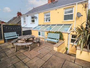 A paved outdoor patio area with wooden benches and a round picnic table at Greengate in Tenby