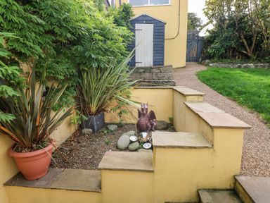 A garden area with potted plants a small statue and a blue shed at Greengate in Tenby